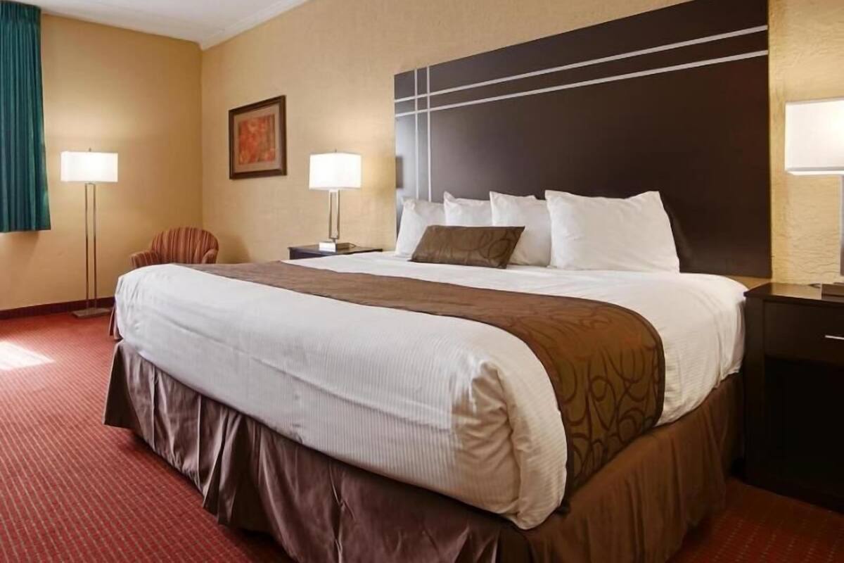 A hotel room with a large bed, two bedside lamps, a chair, and a painting on the wall.