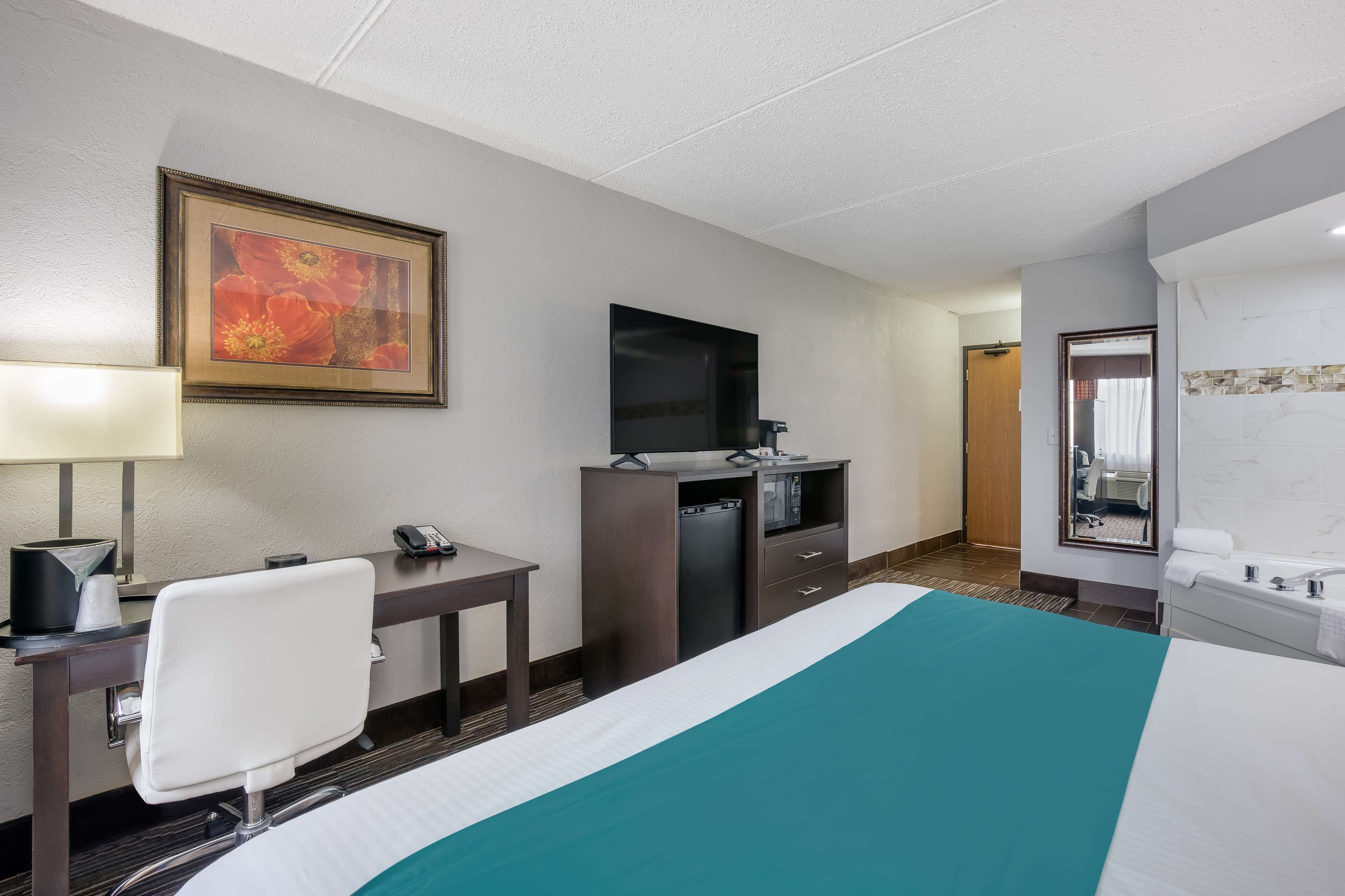 Habitación de hotel con cama, escritorio y silla, televisión, espejo y baño con lavabo y espejo.