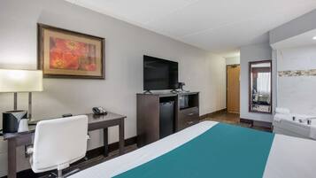 Habitación de hotel con cama, escritorio y silla, televisión, espejo y baño con lavabo y espejo.