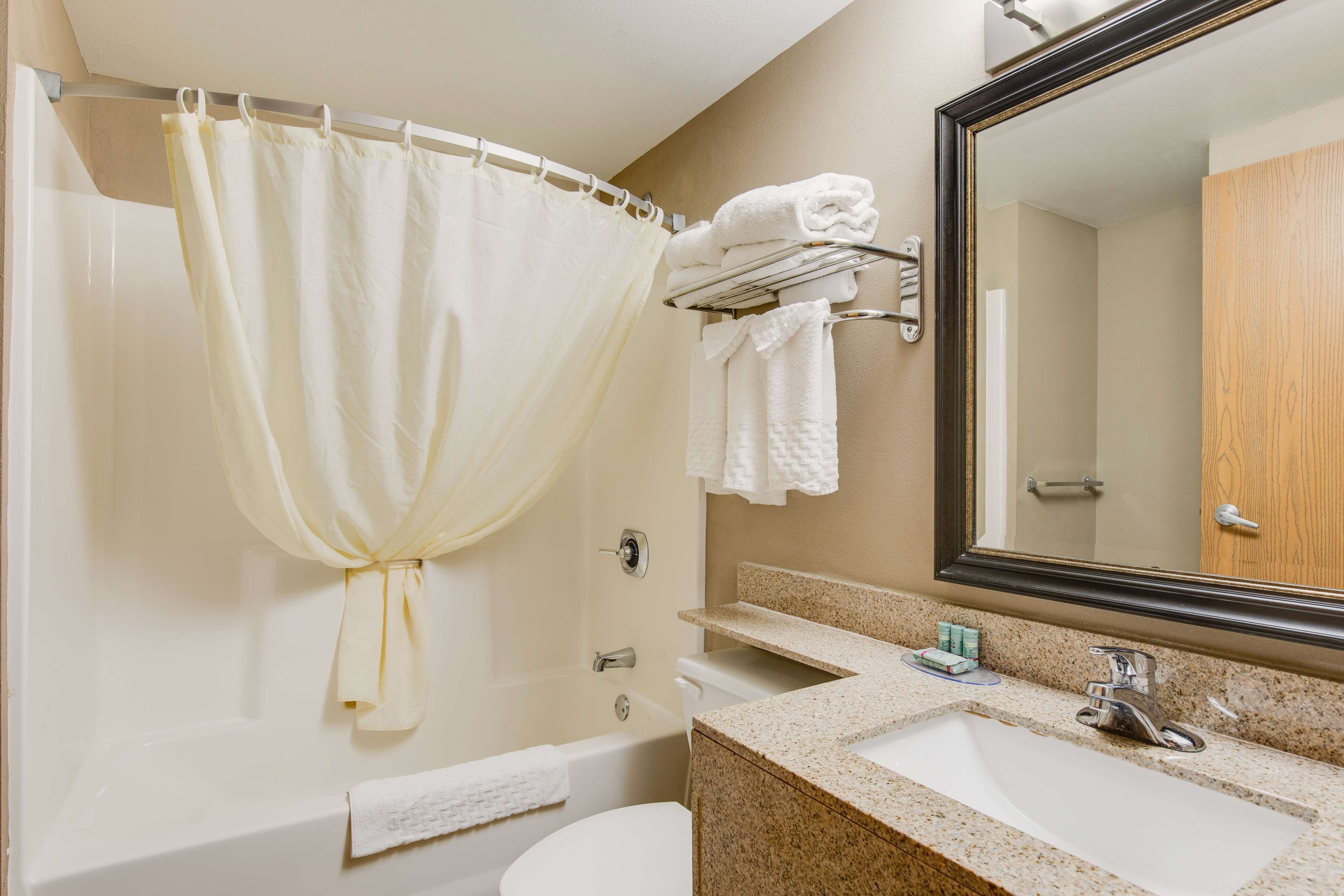 Une salle de bain comprenant une baignoire, un rideau de douche, des toilettes, un lavabo avec un miroir et un porte-serviettes.