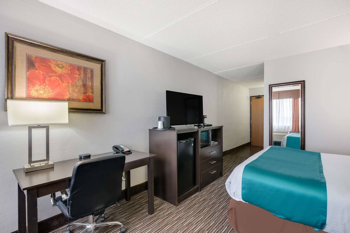 A hotel room with a bed, desk, chair, television, and a minibar.