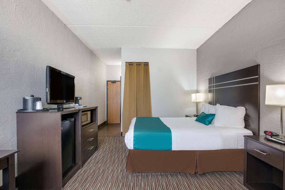 A hotel room with a bed, a desk with a television, a coffee maker, and a nightstand with a lamp.