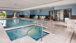 A swimming pool with a tiled deck, a lounge area with chairs, and a view of the outside.