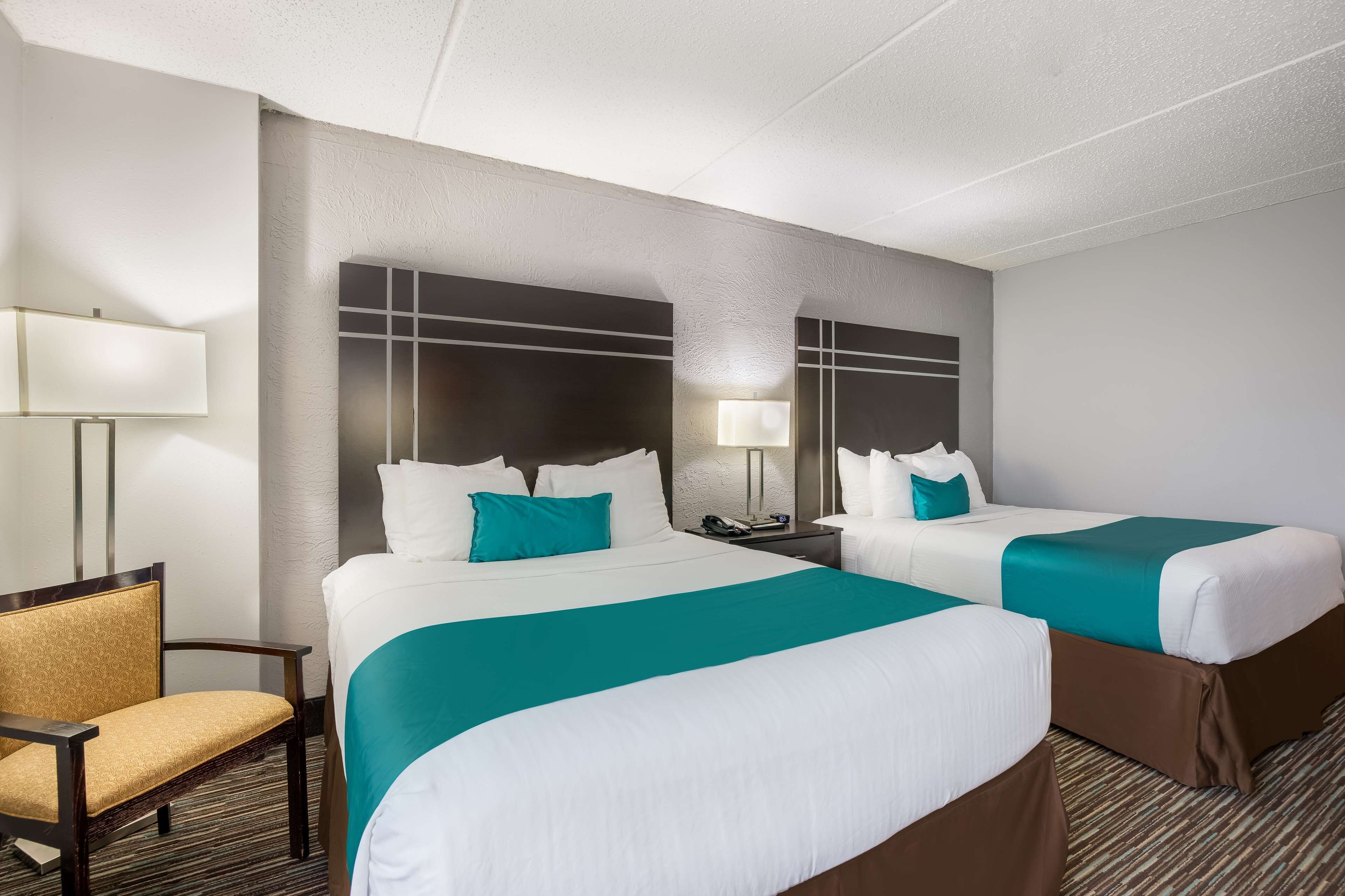 A hotel room with two beds, a chair, a lamp, and a nightstand.