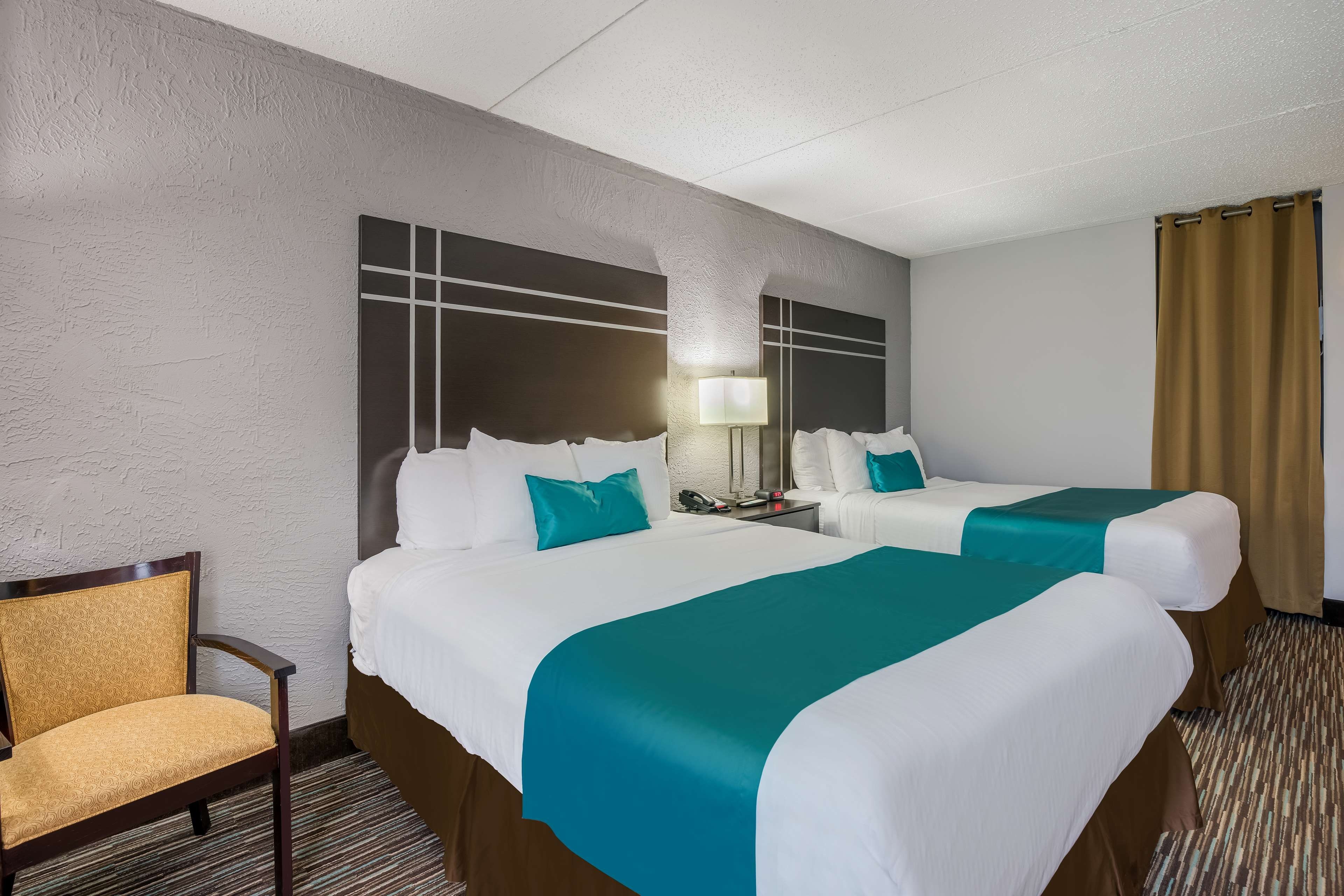 Une chambre d’hôtel avec deux lits, une chaise, une table de chevet et une lampe.