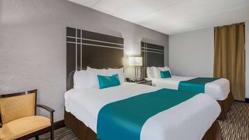 A hotel room with two beds, a chair, a nightstand, and a lamp.
