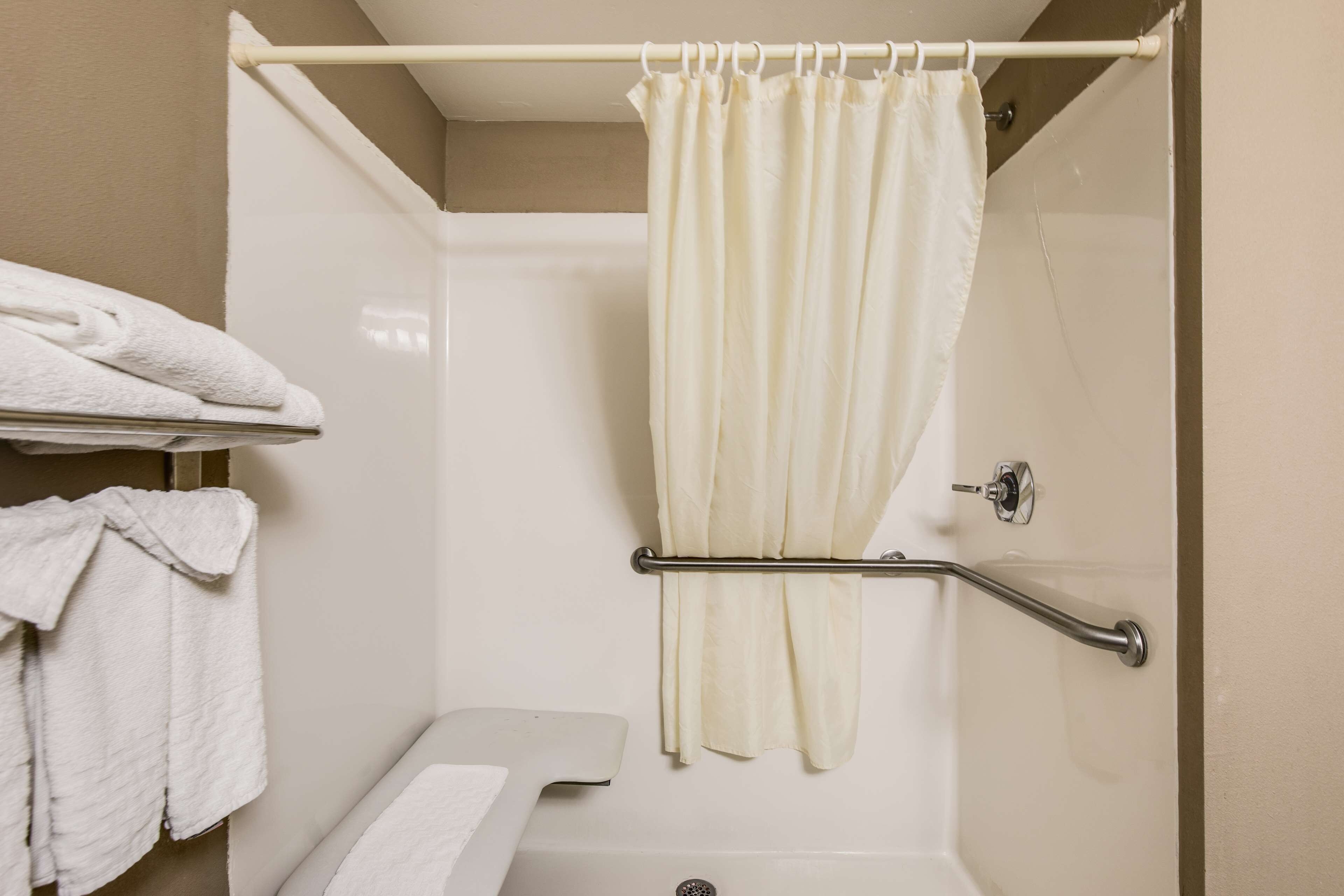 A shower area with a white curtain, a grab bar, and a shelf with folded towels.