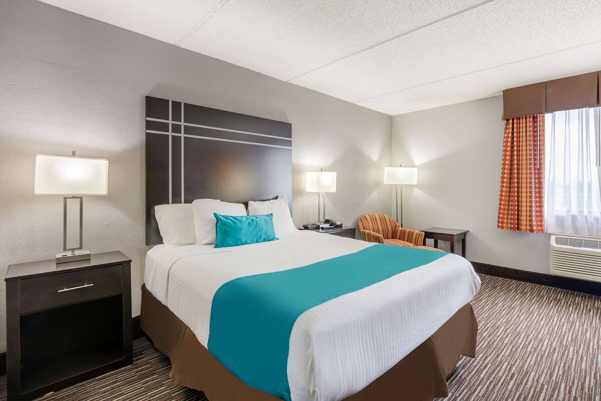 A hotel room with a large bed, two bedside tables with lamps, a chair, and a window with curtains.
