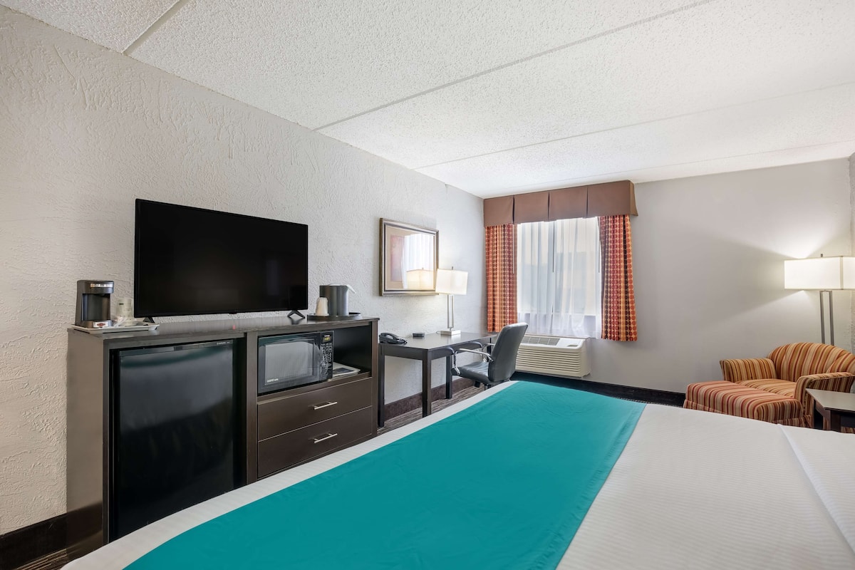 A hotel room with a bed, a desk, a television, a mini-fridge, a lamp, and a window with curtains.