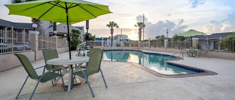 A poolside area with a table and chairs, a green umbrella, and a pool.