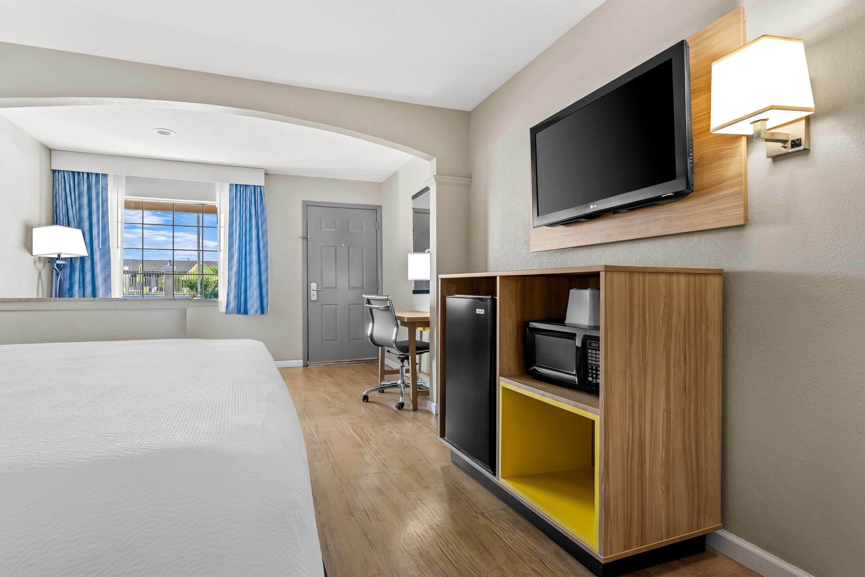A hotel room with a bed, a desk with a chair, a television, and a microwave.