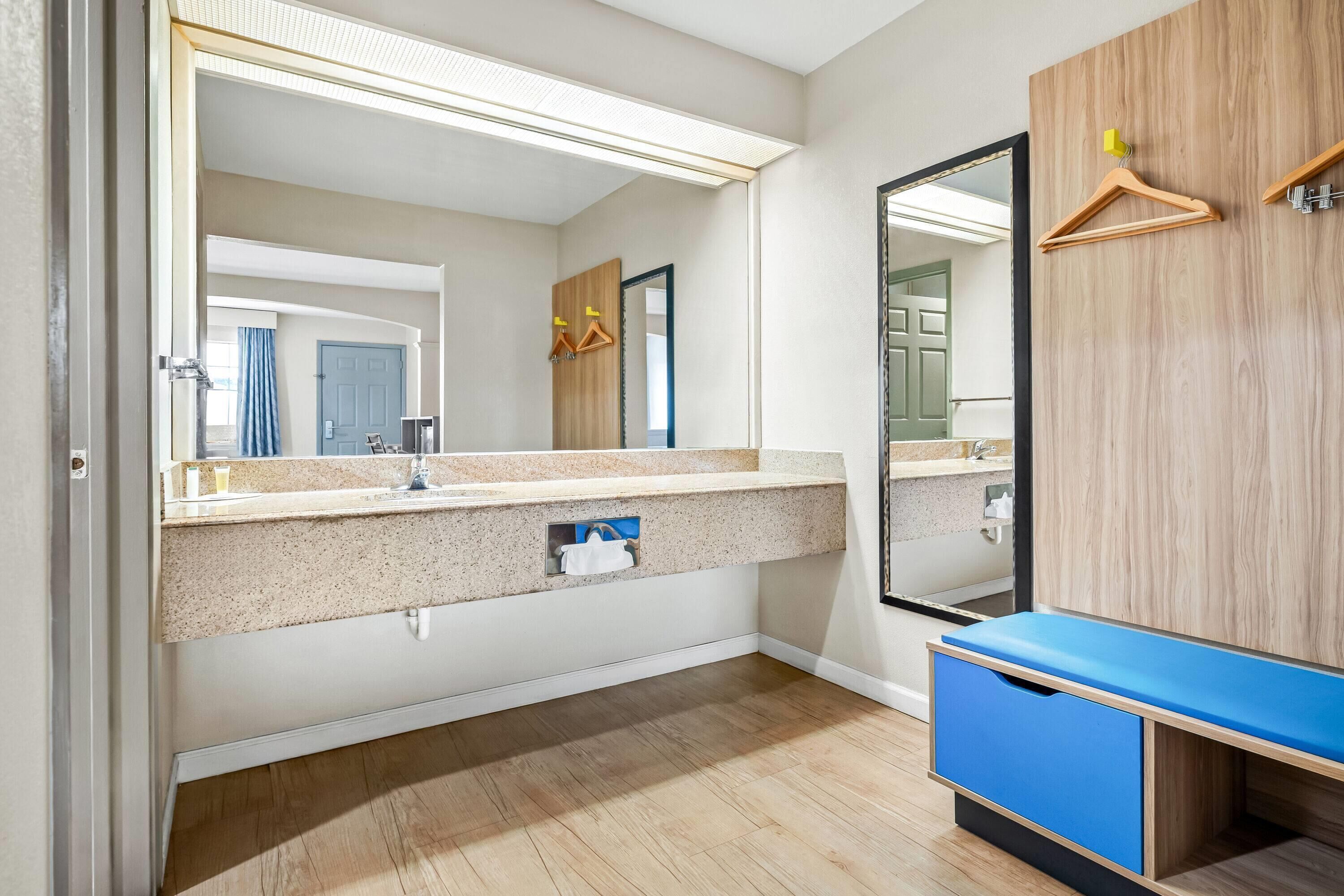 A modern bathroom with a large mirror, a countertop with a sink, and a wooden vanity with a blue drawer.