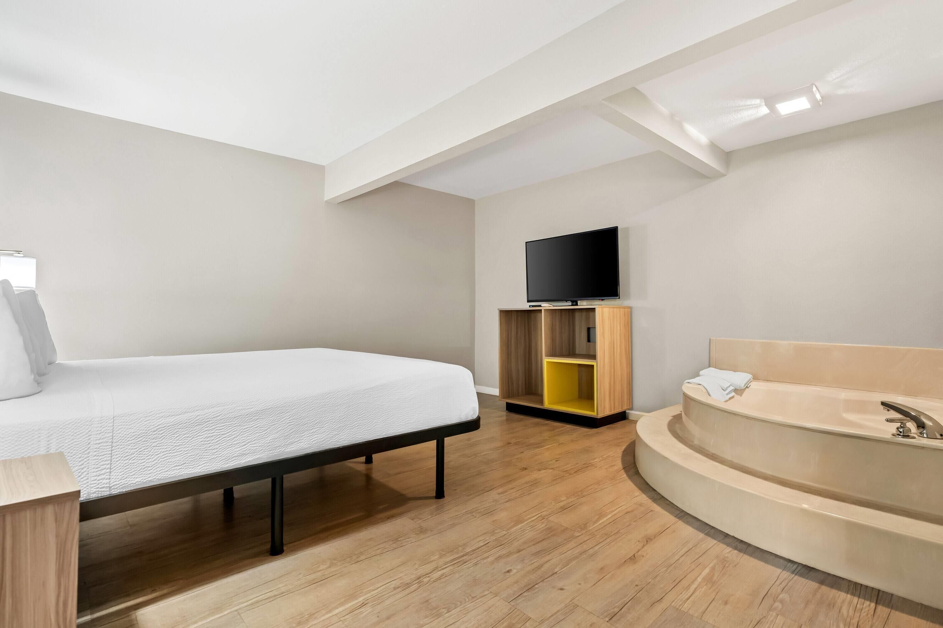 A modern hotel room with a bed, a TV, a wooden cabinet, and a bathtub.