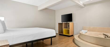 Ett modernt hotellrum med en säng, en TV, ett träskåp och ett badkar.