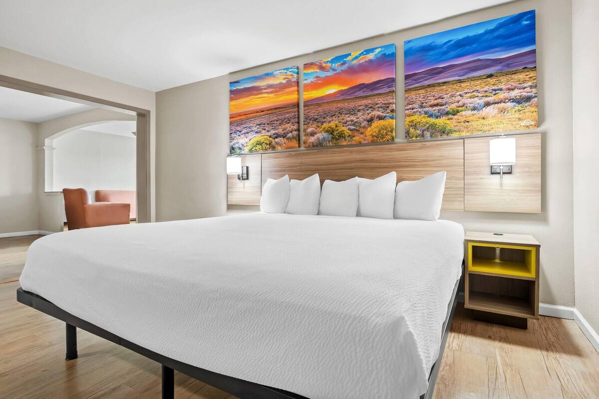 A large bed with white bedding, a wooden headboard, and a nightstand with a yellow shelf.