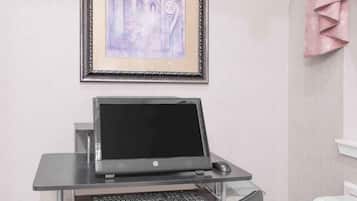 Un ordenador portátil sobre un escritorio de cristal, con teclado y ratón, un cuadro en la pared y un radiador blanco.