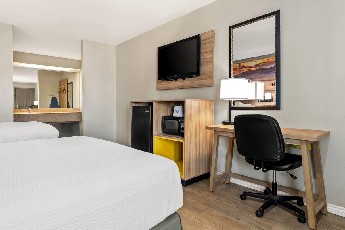 A hotel room with two beds, a desk with a chair, a TV, a microwave, and a small cabinet.