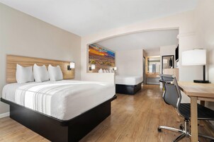Habitación de hotel con una cama grande, un escritorio y una silla. Hay un cuadro en la pared y un espejo sobre el escritorio.
