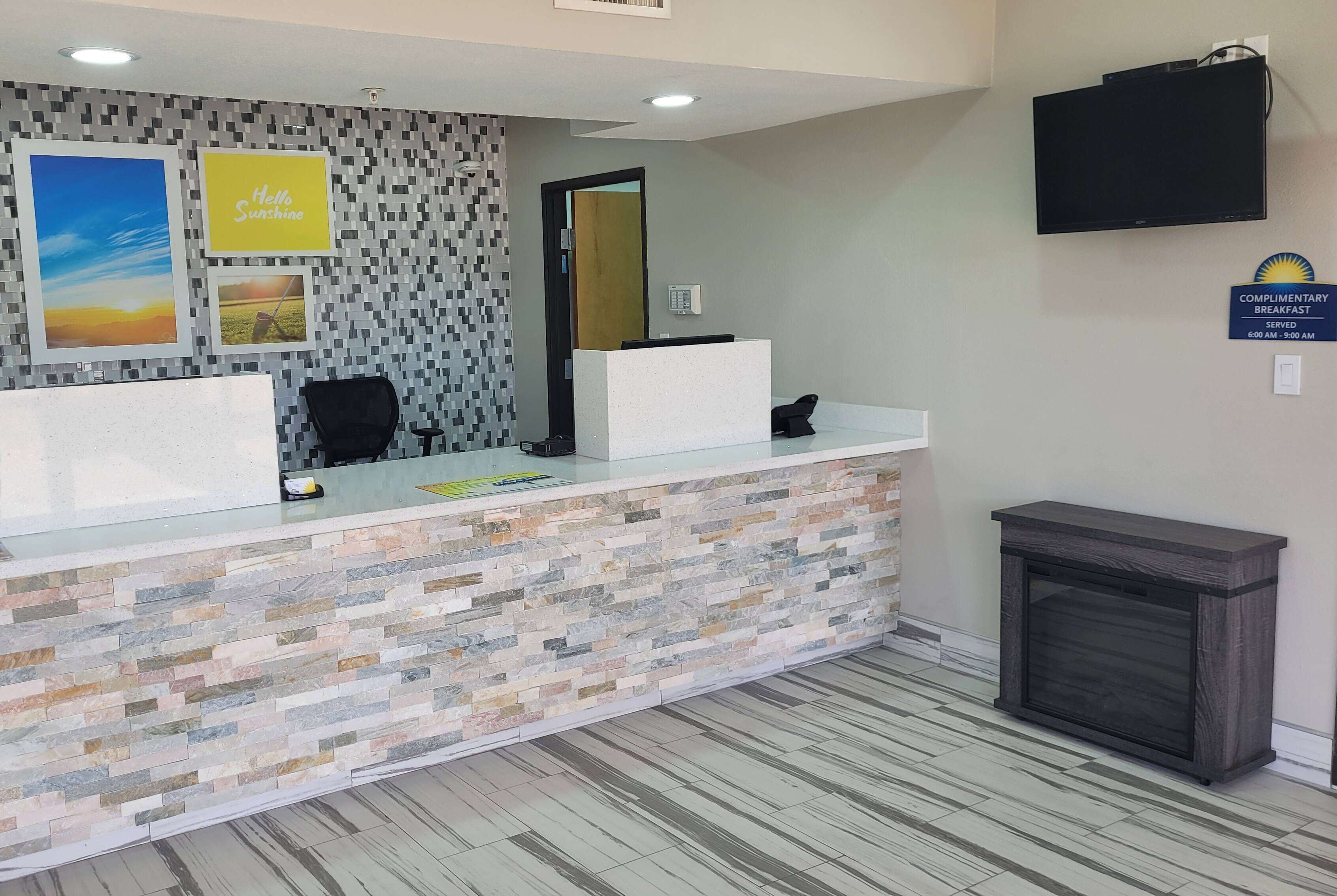 A reception area with a stone-patterned counter, two chairs, a television, and a sign indicating complimentary breakfast hours.