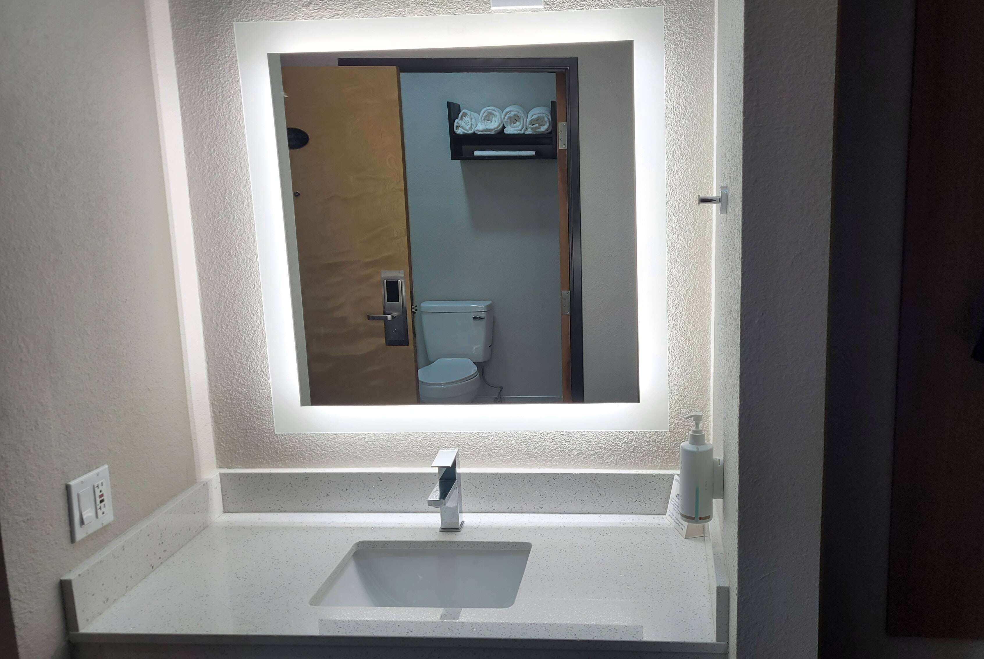 A bathroom with a white sink, a mirror, and a toilet visible through the door.