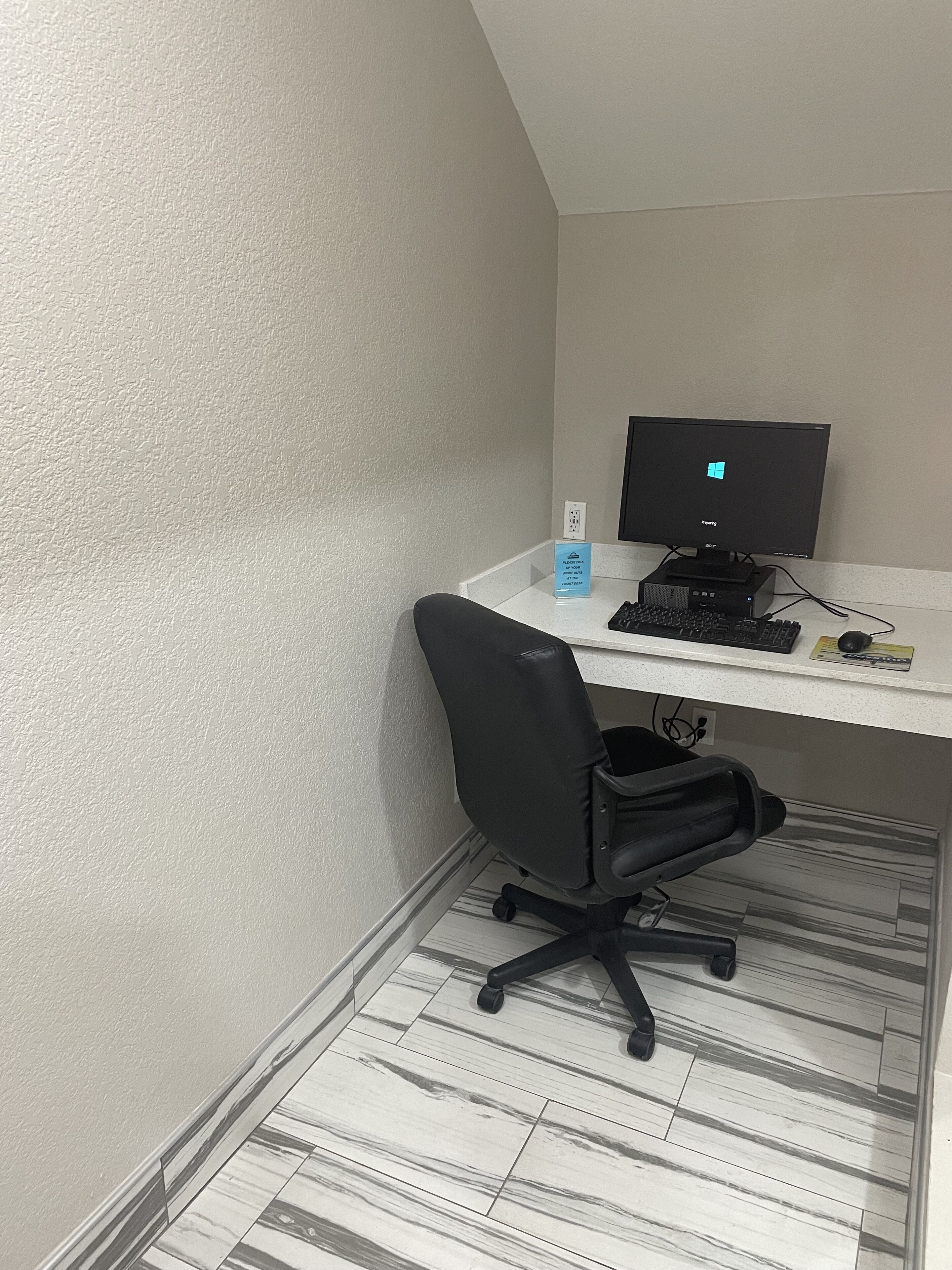 A corner office with a white desk, a black office chair, a computer monitor, and a keyboard.