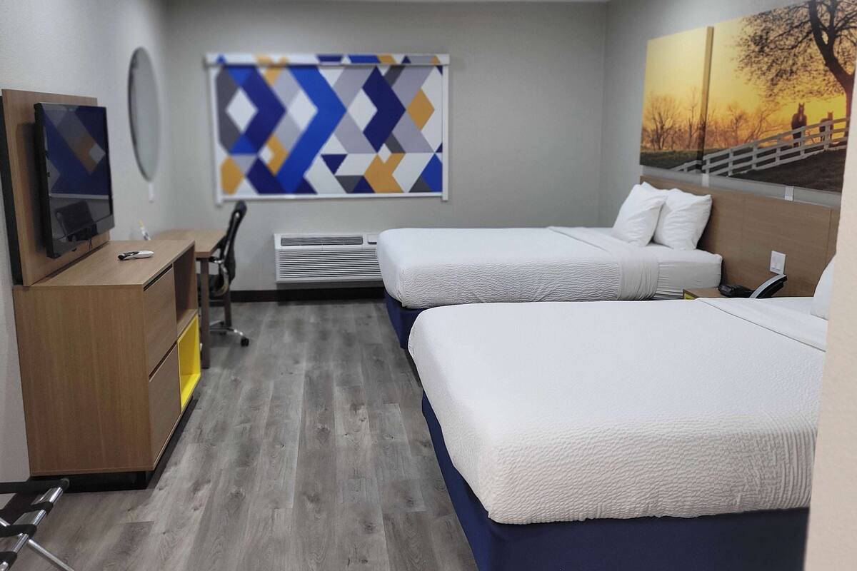 A hotel room with two beds, a desk with a computer, a chair, and a TV.