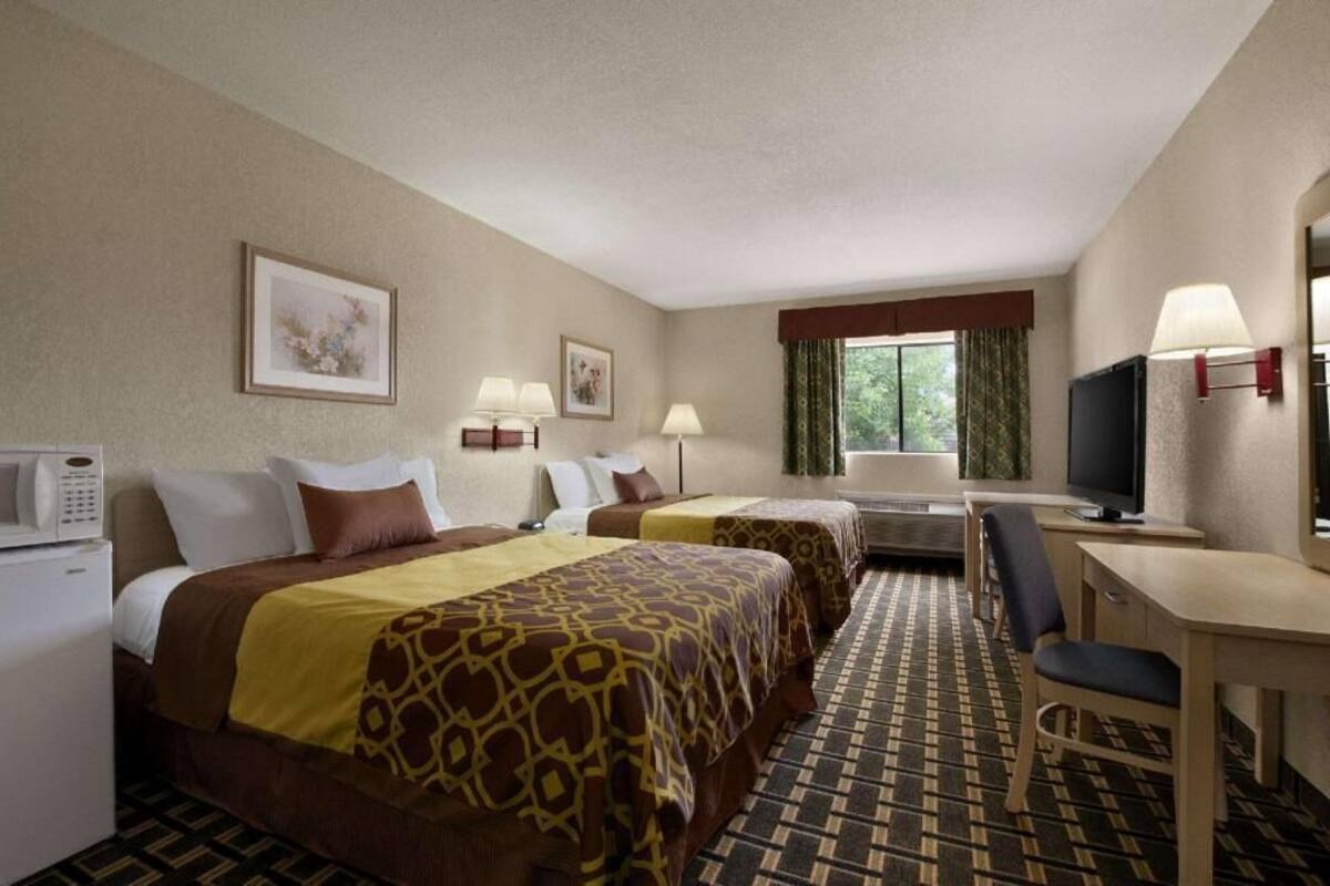 A hotel room with two beds, a desk, a chair, a television, and a microwave.