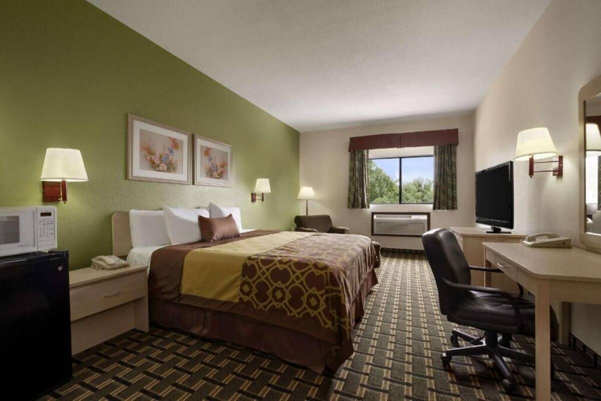A hotel room with a bed, desk, chair, TV, and a microwave.