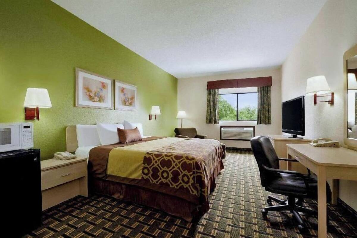 A hotel room with a bed, desk, chair, television, and a window with curtains.