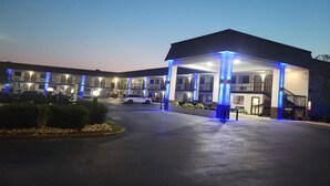A motel with a covered parking area and multiple buildings in the background. - Western Motel Thomasville  (Thomasville)