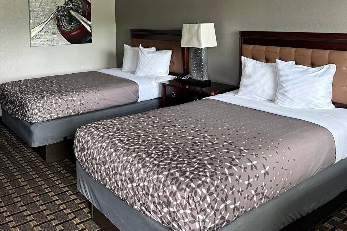 Een hotelkamer met twee bedden, een nachtkastje, een lamp en een schilderij aan de muur.