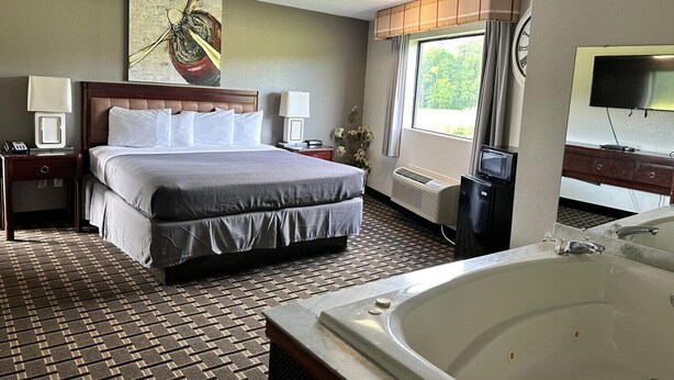 A hotel room with a large bed, a separate bathroom with a bathtub, a television, and a window with curtains. - Western Motel Thomasville  (Thomasville)