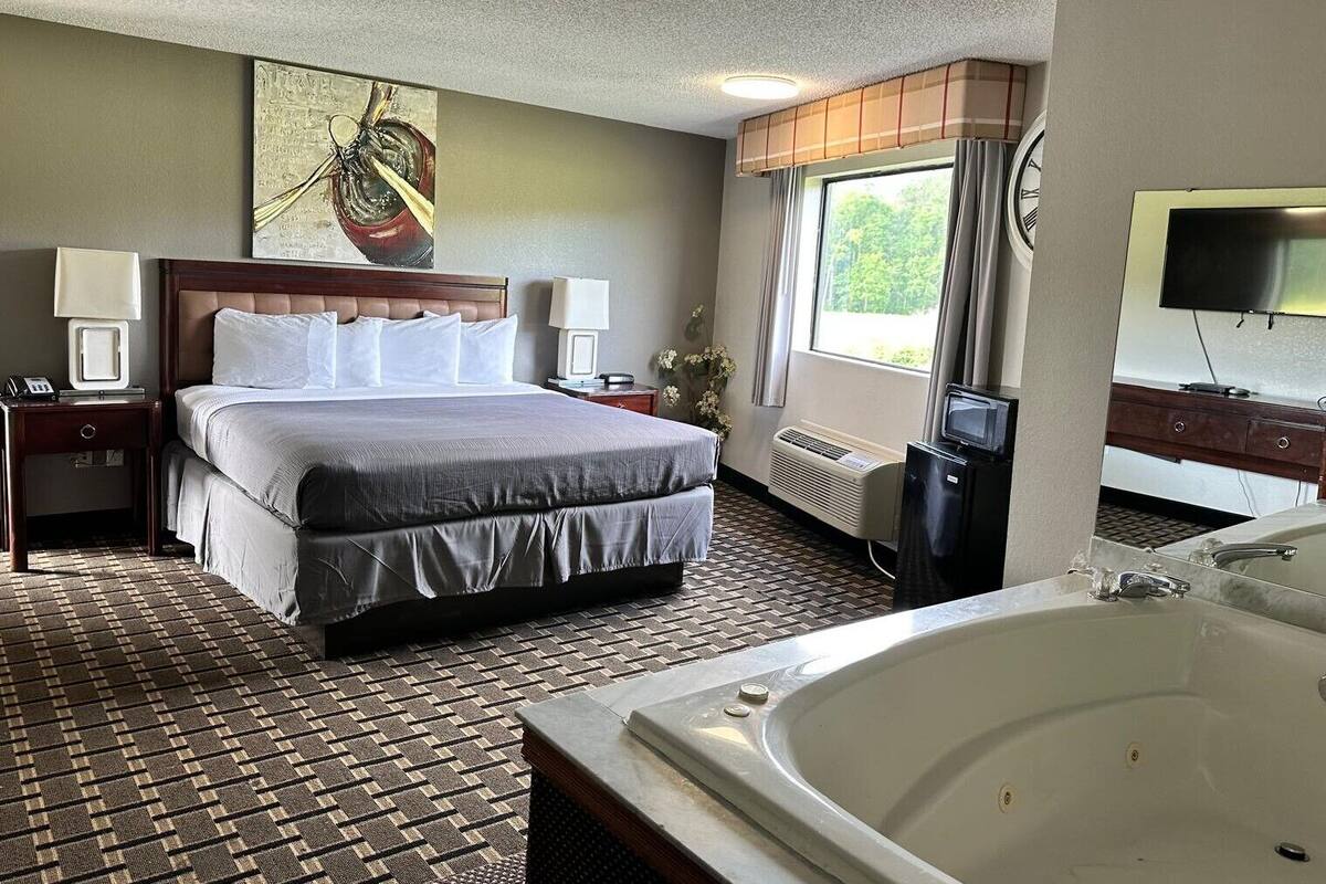 Een hotelkamer met een groot bed, een aparte badkamer met badkuip, een televisie en een raam met gordijnen.