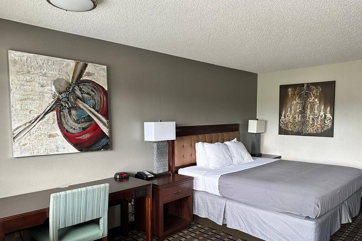 Een hotelkamer met een bed, een bureau, een stoel, een lamp en twee kunstwerken aan de muur.