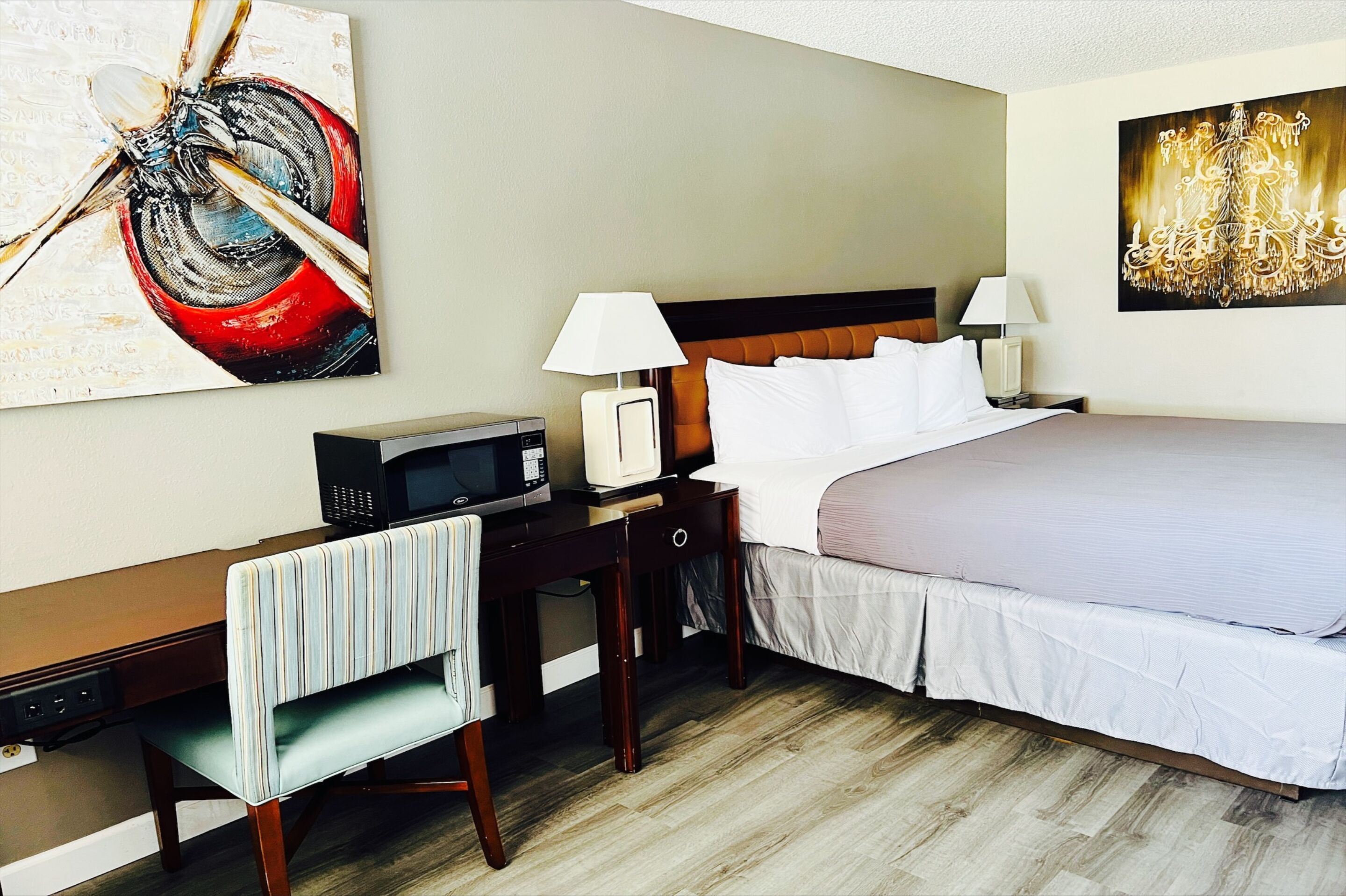 Habitación de hotel con una cama, mesitas de noche, un escritorio, una silla, un microondas y dos cuadros en las paredes.