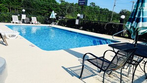 A swimming pool with lounge chairs and umbrellas, surrounded by a fence and greenery. - Western Motel Thomasville  (Thomasville)