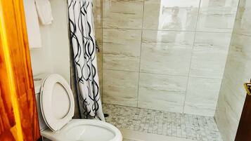 Et badeværelse med toilet, en bruser med et mønstret gardin og et flisegulv.