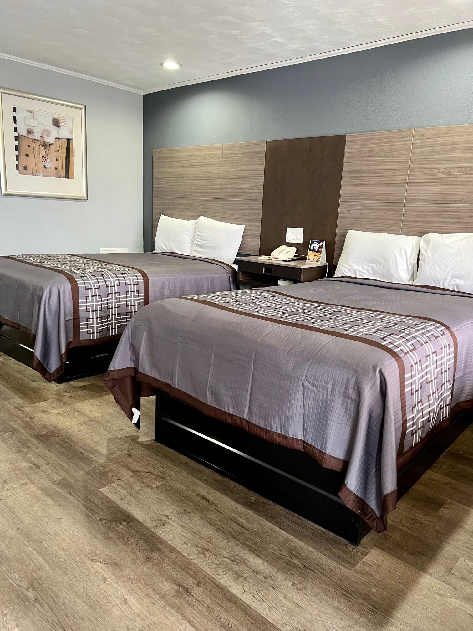 Ein Hotelzimmer mit zwei Betten, einem Holz-Kopfteil, einem Nachttisch mit Telefon und einem gerahmten Bild an der Wand.