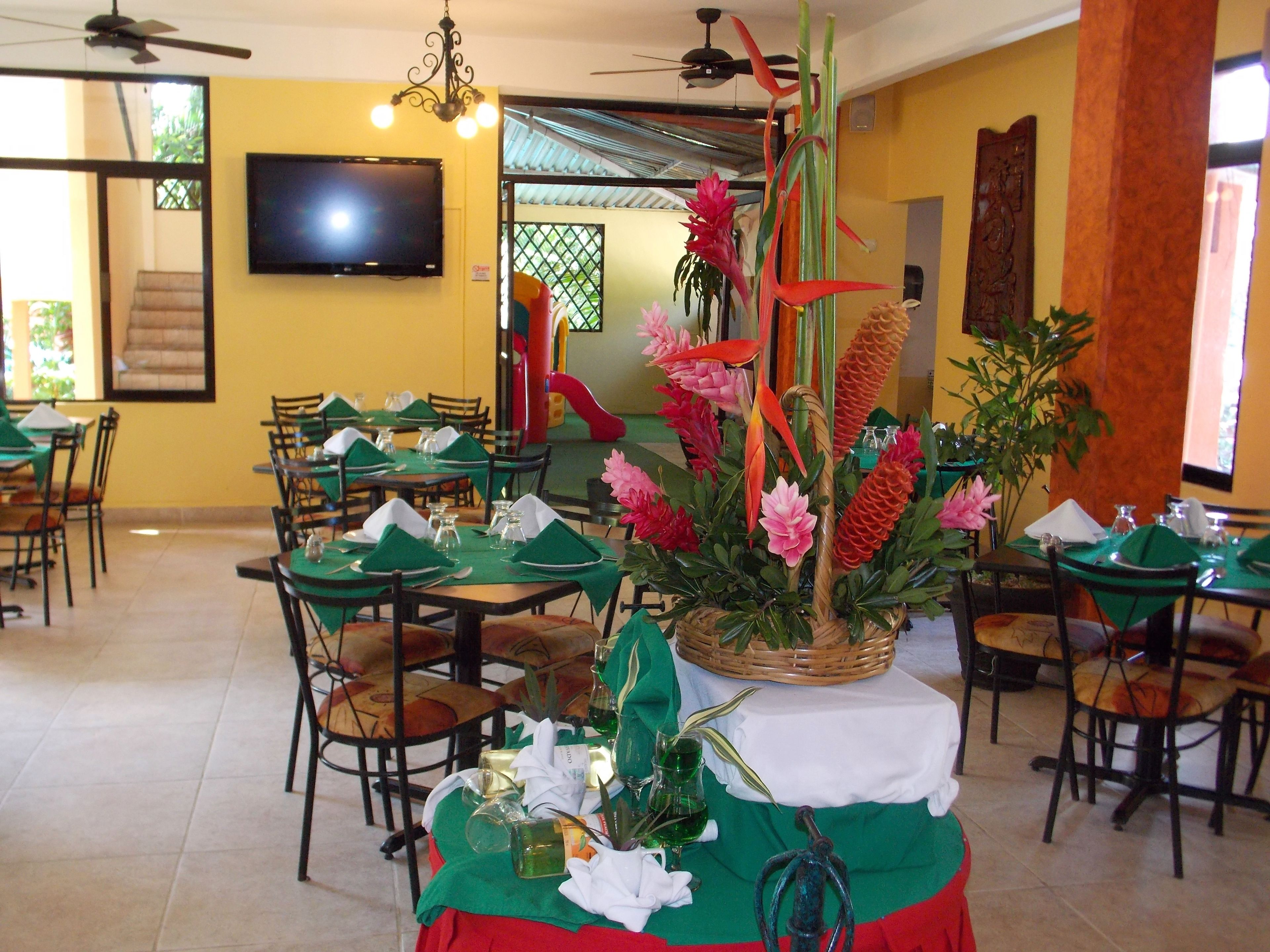A restaurant with tables set for dining, a television mounted on the wall, and a staircase leading to an upper level.