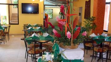A restaurant with tables set for dining, a television mounted on the wall, and a staircase leading to an upper level.
