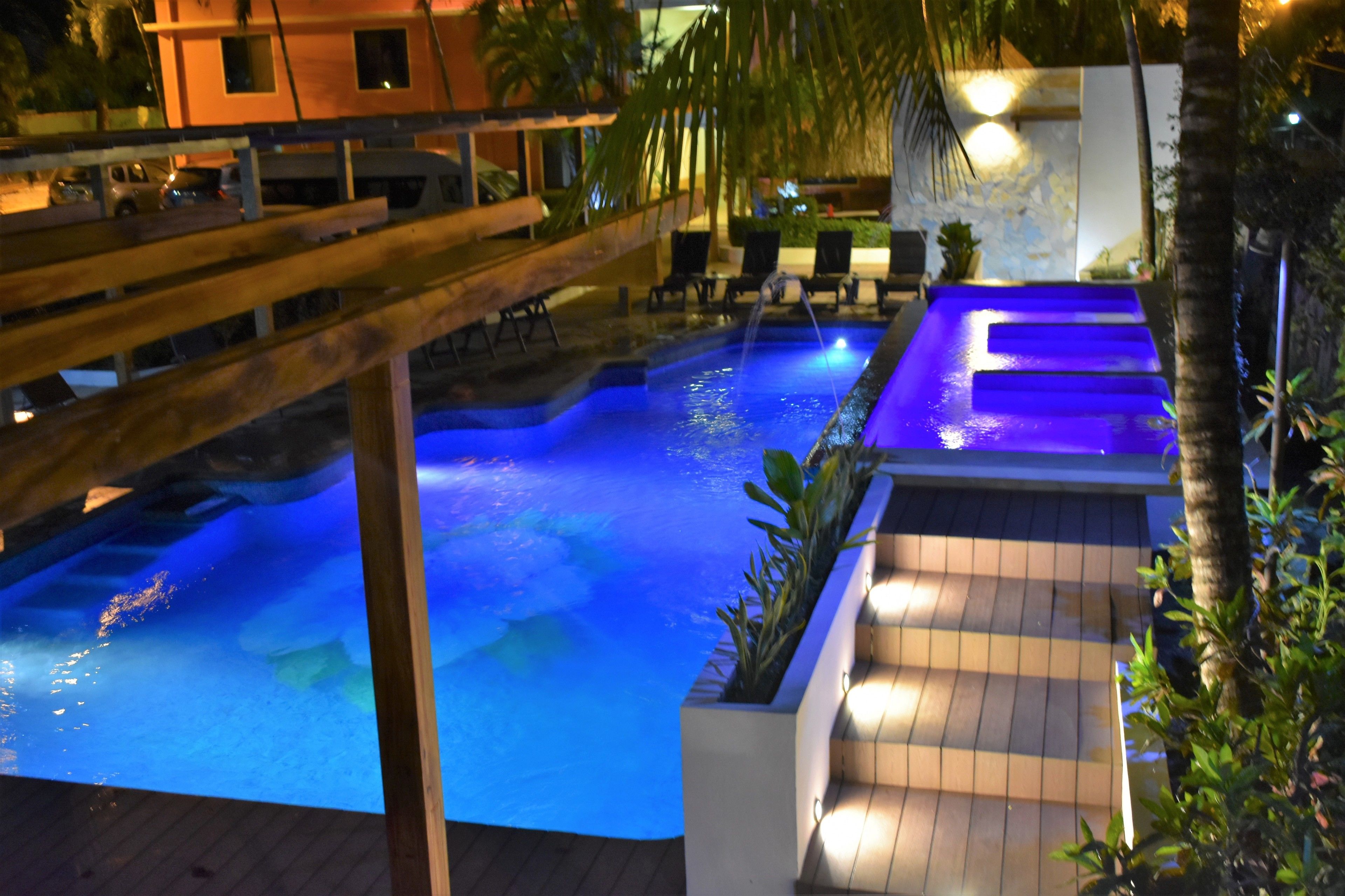 A swimming pool with blue lighting, wooden deck, and lounge chairs.