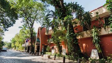 Une rue pavée bordée d’arbres et un bâtiment à la façade rouge.