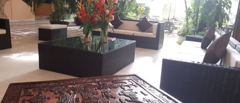 A modern indoor space with a glass coffee table, wicker furniture, and a decorative wooden panel.