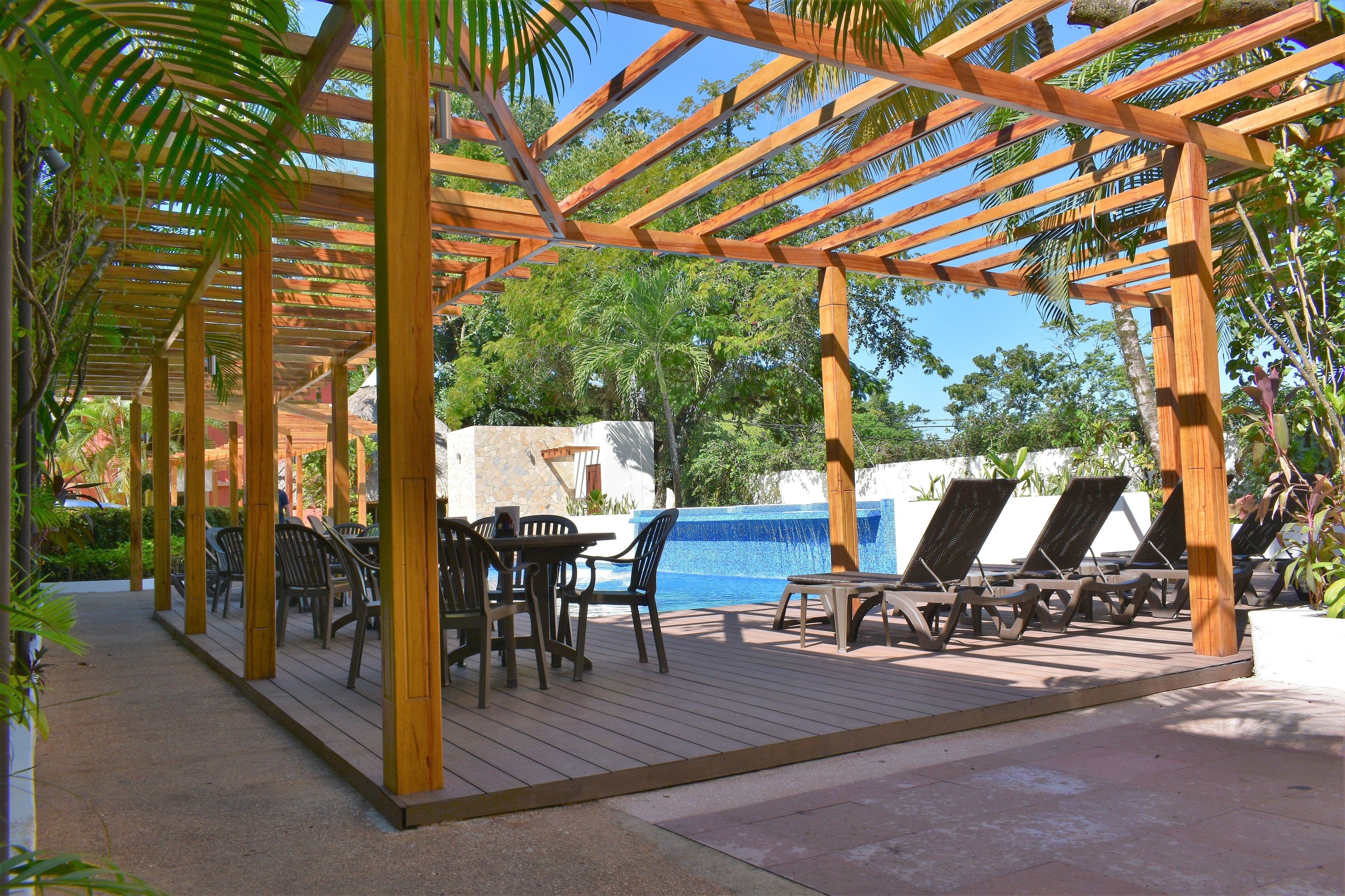A wooden pergola with a pool area, including lounge chairs and a table with chairs.