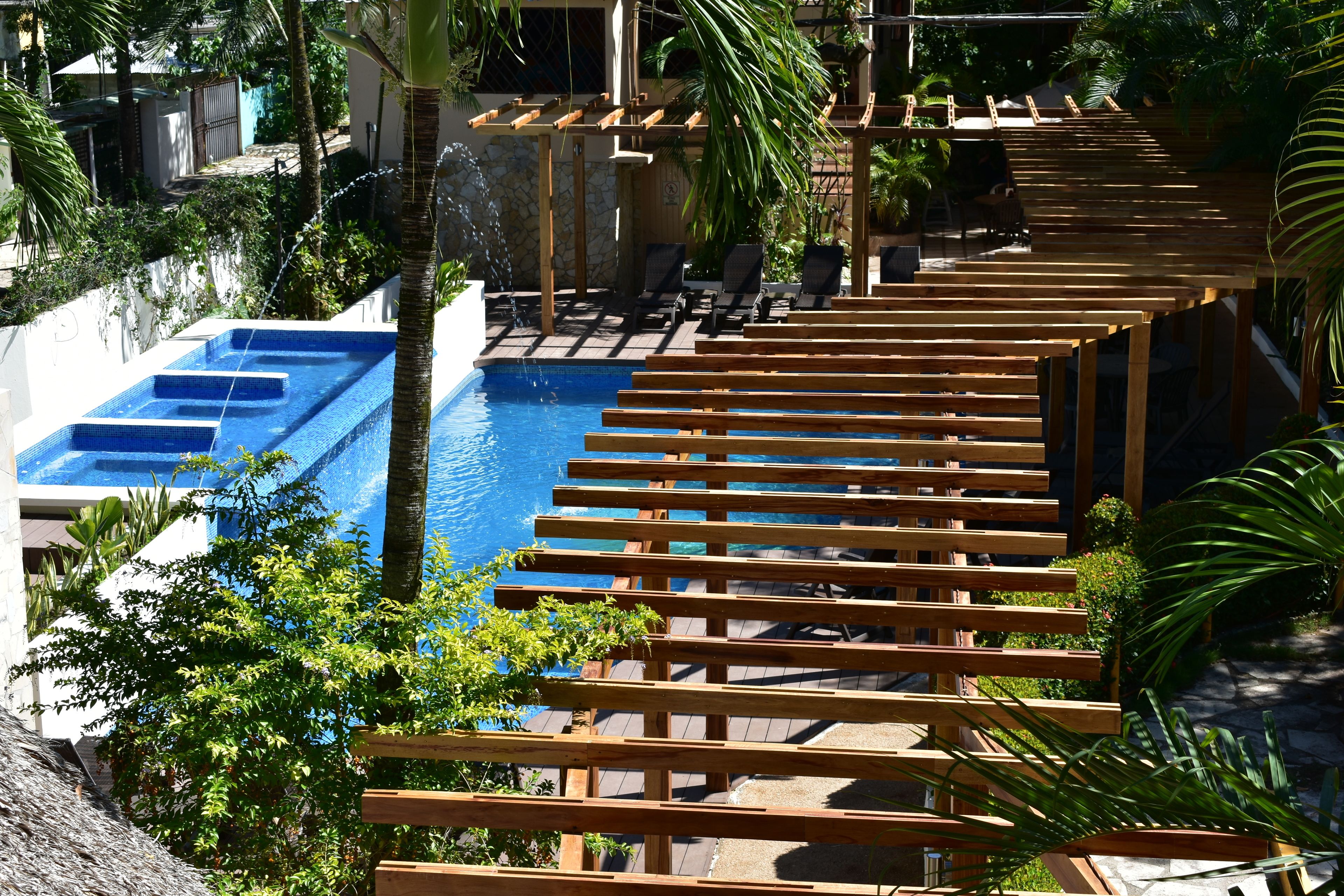 A pool area with wooden pergolas, lounge chairs, and a clear blue pool.