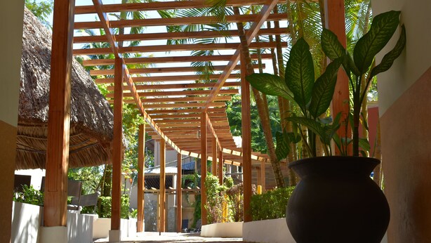 Uma galeria coberta com vigas de madeira e um vaso grande com planta.