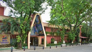 Entrada de hotel com um mural colorido, rodeada por vegetação exuberante e um caminho pavimentado.