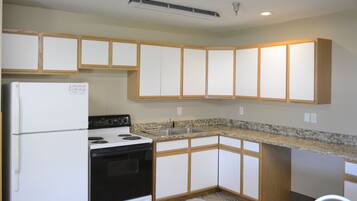 Una cocina con armarios blancos, una estufa negra y un refrigerador blanco.