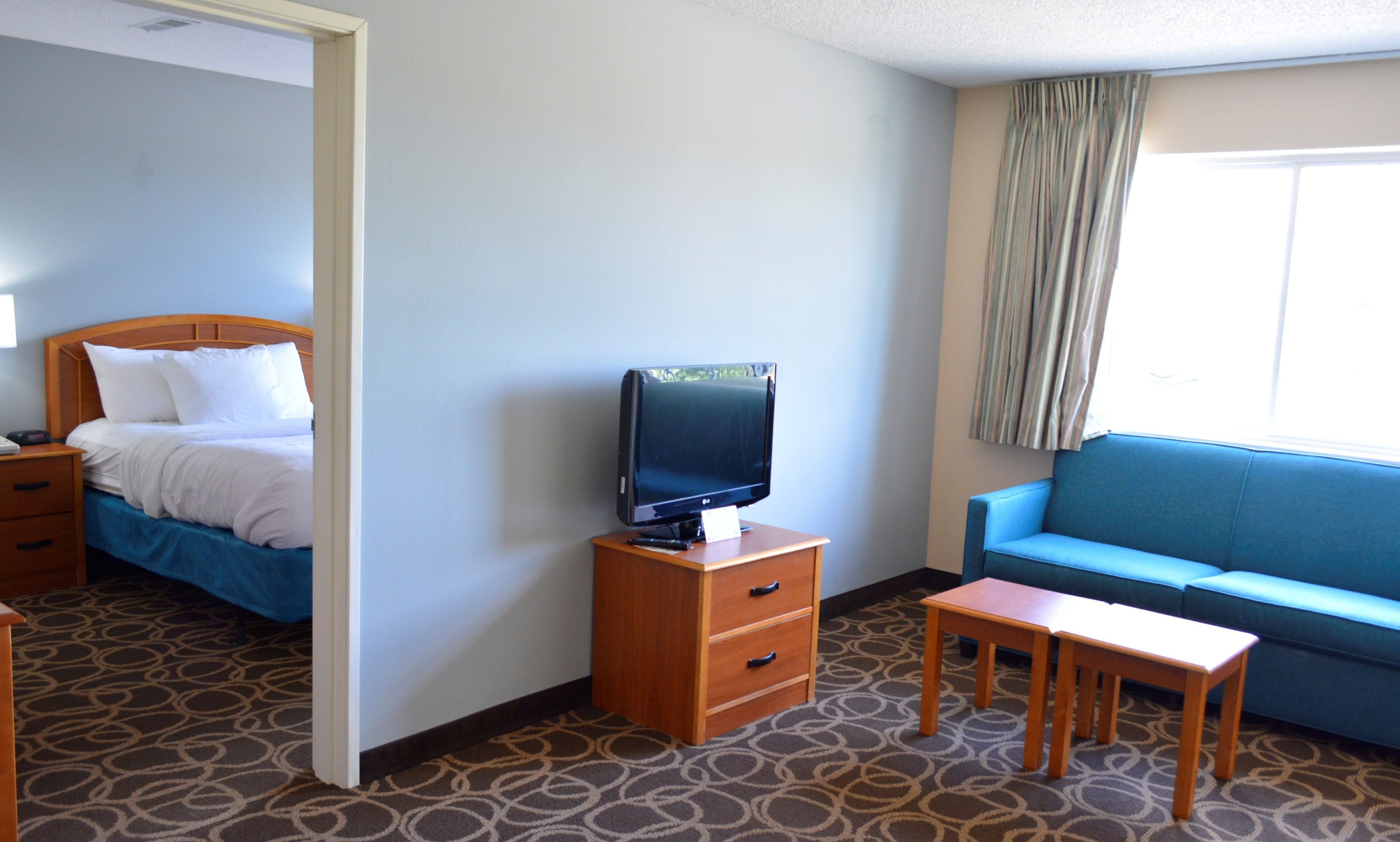 Ein Hotelzimmer mit einem Bett, einem Fernseher auf einem Holzboden, einem blauen Sofa und einem kleinen Tisch.