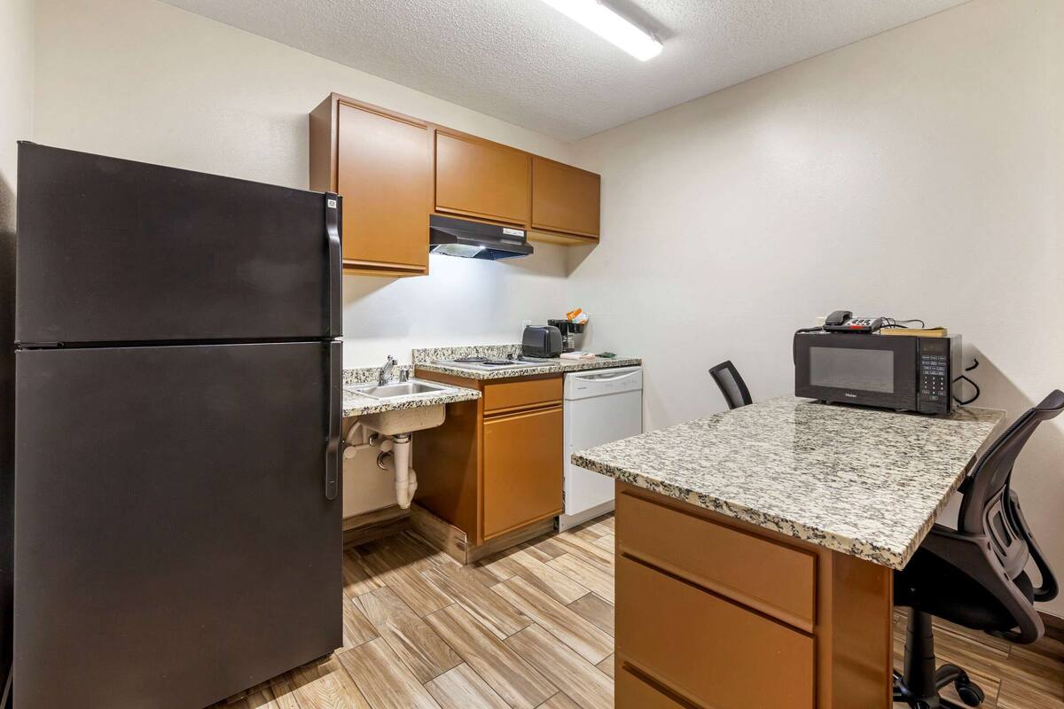 A compact kitchen with a refrigerator, dishwasher, microwave, and granite countertop.